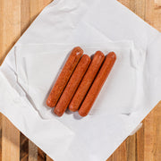 Porter Road Butcher | Dry Aged Hot Dogs: A close-up of four flavorful, dry-aged beef hot dogs, seasoned with garlic and spices, displayed on a napkin.