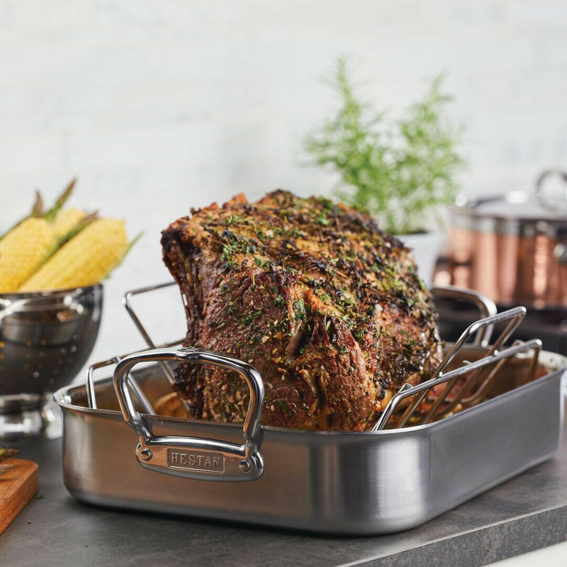 Hestan Provisions Classic Roaster with Rack holding a herb-crusted beef roast, highlighting its 16.5-inch stainless steel design for versatile cooking.