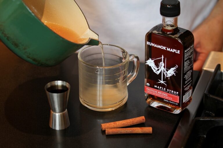 Runamok | Maple Syrups - Festivus Spice Infused, showcased with syrup being poured into a glass beside a liquor bottle, highlighting its culinary versatility.