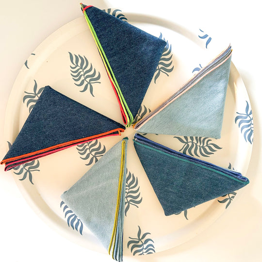 Tisch New York | Chambray Napkins with Pink Hem Set of 4 displayed folded on a plate, showcasing their craftsmanship and pre-washed cotton texture.