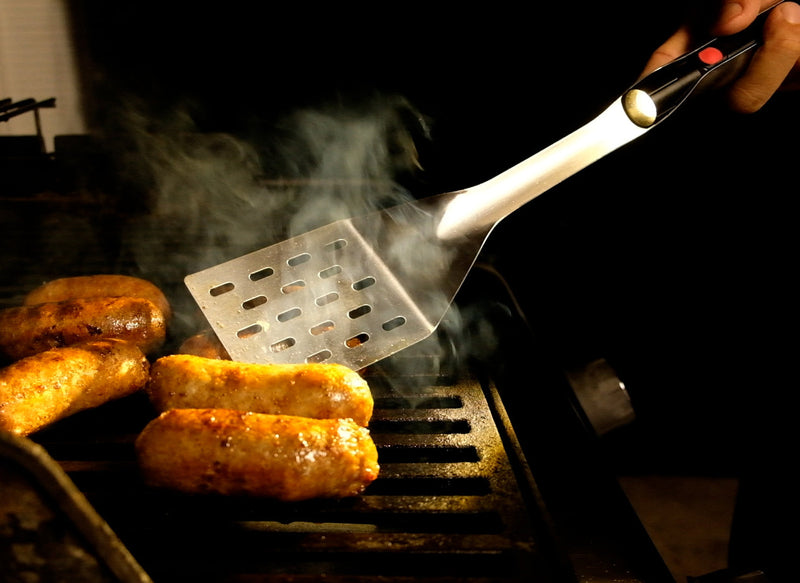 GrilLight | Gift Set - 2 Piece Spatula + Tongs shown grilling sausages, featuring LED lights for optimal evening cooking. Ideal for barbecue enthusiasts.