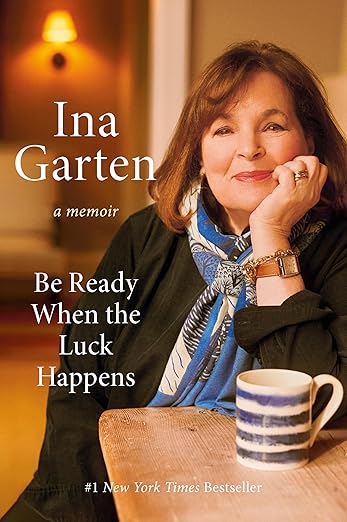 Ina Garten's memoir Be Ready When the Luck Happens features her at a table with a mug, reflecting her culinary journey.