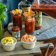 Large J.K. Adams Round Ash Serving Board displaying a shrimp-garnished Bloody Mary cocktail setup, featuring Tito’s vodka, Granny Blossom’s mix, and Vermont Made Sriracha.