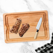 J.K. Adams | Maple BBQ Carving Board with steaks and knife, showcasing its groove for juice collection and ideal carving surface, on a marble countertop.
