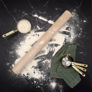 J.K. Adams | Plain Dowel Rolling Pin on flour-dusted countertop with brass and metallic measuring cups, highlighting its classic design and utility for baking tasks.