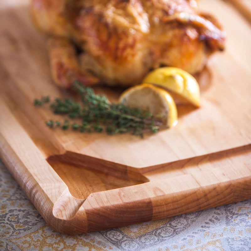 J.K. Adams Maple Reversible Pour Spout Carving Board with roasted chicken, lemon wedges, and thyme, showcasing its juice groove and spout feature.