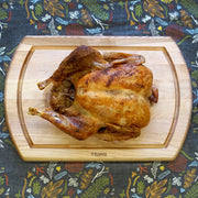 J.K. Adams | Maple Reversible Carving Board holding a whole roasted chicken, showcasing its indentation feature for stable carving.