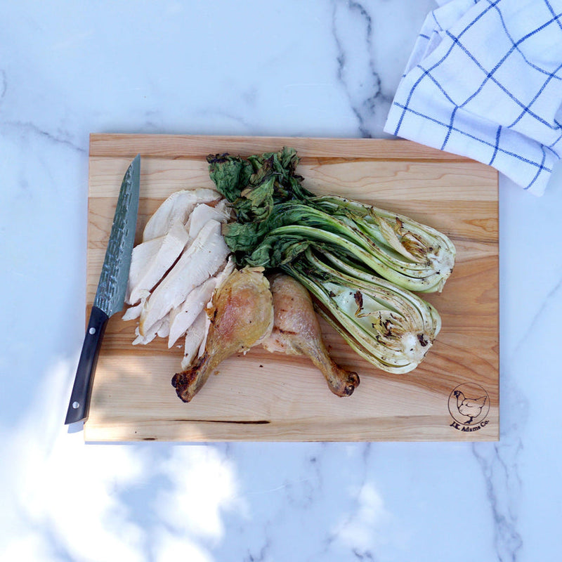 J.K. Adams | Maple Reversible Prep Boards, 16 x 12 inches, displaying chicken and veggies on a marble countertop, with a chef’s knife and checkered towel.