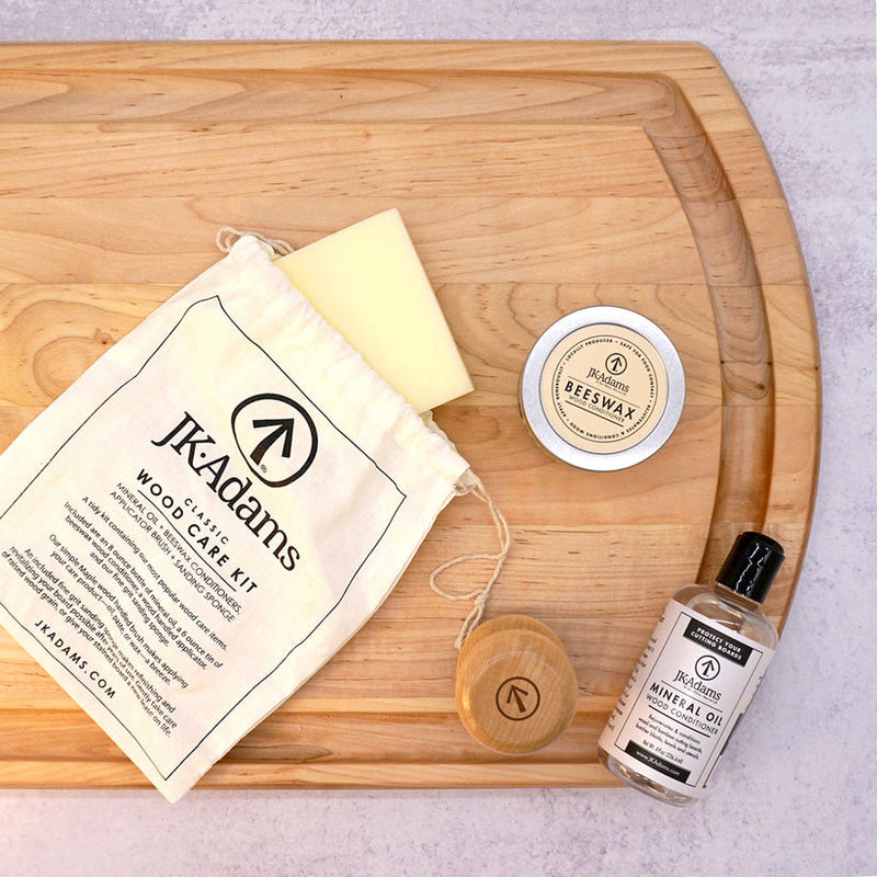 JK Adams Classic Wood Care Kit on a cutting board, featuring a canvas pouch, mineral oil, beeswax tin, applicator puck, and conditioning sponge.