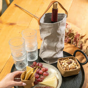 UASHMAMA Wine Bag Carrying Tote with Cooler in denim, featuring a leather strap, stylishly holds a wine bottle beside cheese, grapes, and crackers on a table.
