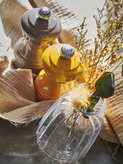 Peugeot | Bistro Pepper Mill in saffron and dark gray, paired with a ribbed vase of dried grasses on a natural cloth, in warm light.