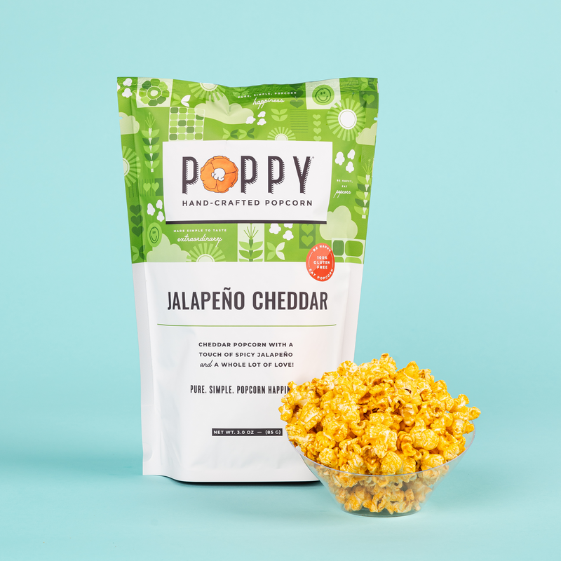 Poppy | Handcrafted Popcorns - Jalapeño Cheddar: A bowl of spicy, cheesy popcorn beside a branded bag, highlighting its crunchy texture and jalapeño flavor.