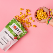 Poppy | Handcrafted Popcorns - Jalapeño Cheddar, a bag of spicy, cheesy popcorn, held in a hand, showcasing its crunchy texture.