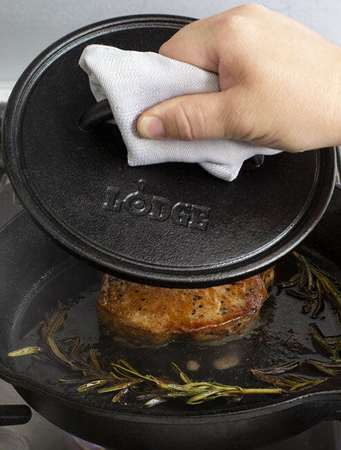 Lodge | Cast Iron Grill Presses - 8 Round being used to flatten a piece of meat in a pan, showcasing its effectiveness in cooking.
