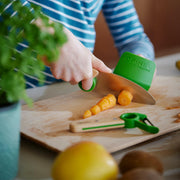 Opinel | Le Petit Chef 3pc Knife Set - Navy: Close-up of a finger guard and chef's knife slicing a carrot on a cutting board, highlighting safe cooking for children.