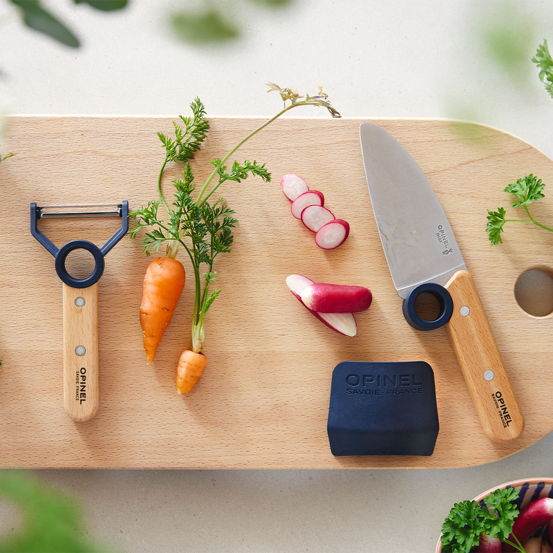 Opinel | Le Petit Chef 3pc Knife Set, Navy, featuring a vegetable peeler, paring knife, and knife-sharpener, arranged with fresh produce on a cutting board.
