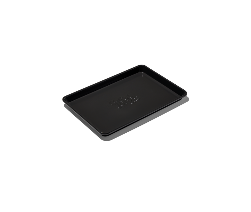 Great Jones | Little Sheet - Pepper, a nonstick quarter-sized baking tray with holes, ideal for small ovens, shown in a close-up emphasizing its design and functionality.