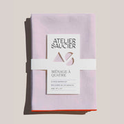 Atelier Saucier | Blush Linen Orange Napkins, Set of 4: Soft, neatly folded, pale-pink napkins with bright orange edges, wrapped in branded paper band.