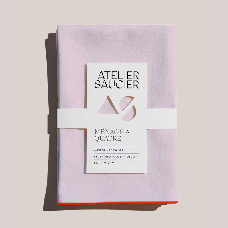 Atelier Saucier | Blush Linen Orange Napkins, Set of 4: Soft, neatly folded, pale-pink napkins with bright orange edges, wrapped in branded paper band.