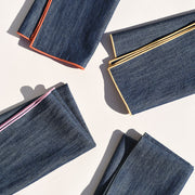 Atelier Saucier | Rainbow Denim Napkins, Set of 4, showcasing neatly folded dark blue denim with vibrant orange, yellow, pink, and green edges, perfect for adding color to your dining experience.