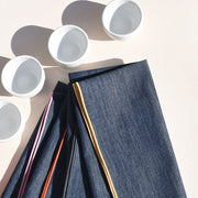 Atelier Saucier | Rainbow Denim Napkins, Set of 4, featuring colorful edges, stacked beneath four white ceramic bowls, perfect for adding fun to your dining experience.