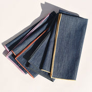 Atelier Saucier | Rainbow Denim Napkins, Set of 4: Dark-blue denim squares with vibrant rainbow edges, combining elegance with playful charm for your dining experience.