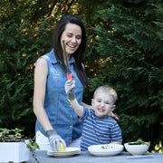 Woman and boy in garden using Microplane Cut Resistant Kitchen Safety Gloves for Kids while preparing food at a stone table with dishes and herbs.
