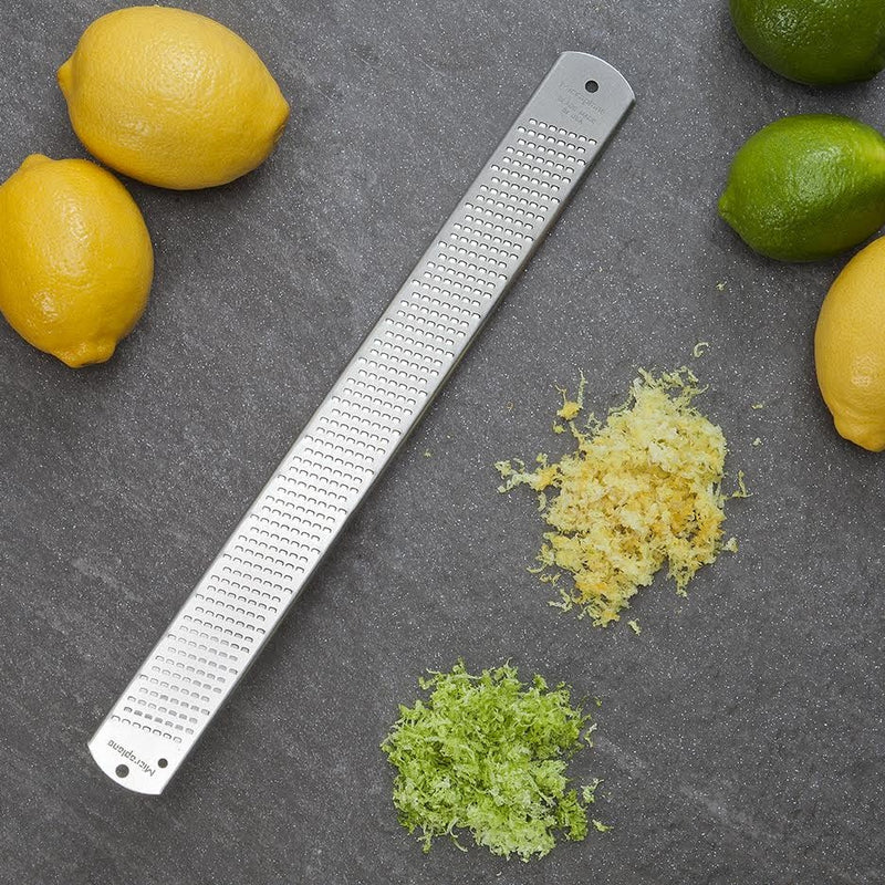 Microplane | Classic Series Stainless Steel Zester on countertop with lemons, limes, and citrus zest piles, showcasing its zesting precision and efficiency for culinary use.