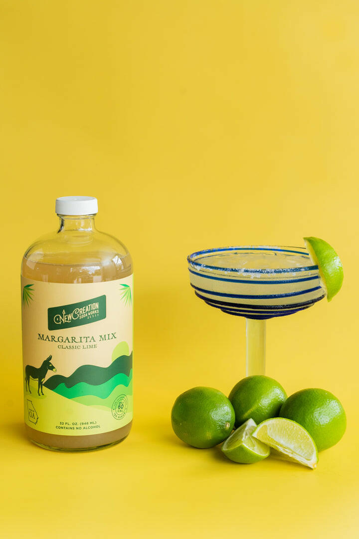 New Creation Soda Works | Margarita Mixes - Classic Lime features organic lime juice in a bottle, accompanied by fresh lime imagery, perfect for crafting simple, flavorful margaritas.