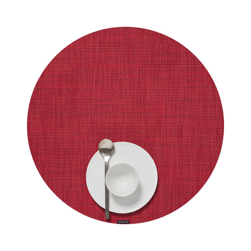 Chilewich | Mini Basketweave Round Placemat, Scarlet, displayed with a white dinner plate, bowl, and silver spoon, showcasing its textured design in a simple table setting.