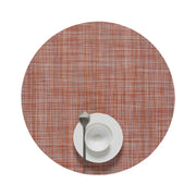 Chilewich | Mini Basketweave Round Placemats, Cinnamon, with a woven texture, featuring a white bowl on a saucer and a teaspoon on the placemat.