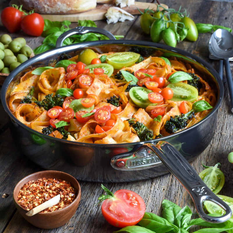 Hestan NanoBond Cookware, 5qt Sauté Pan with lid, showcasing ribbon pasta in tomato sauce, cherry tomatoes, and basil, surrounded by olives, bread, and spices.