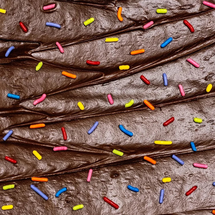 Supernatural | Dye-Free Softies Sprinkles: Diagonal swirls of chocolate frosting adorned with bright, plant-based rainbow sprinkles, highlighting allergy-friendly, vegan, and fair trade attributes.
