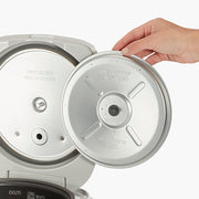 Hand lifting inner lid of Zojirushi | Micom Rice Cooker Warmer - Stainless Gray, highlighting metal insert with usage instructions, showcasing durable design for kitchen efficiency.