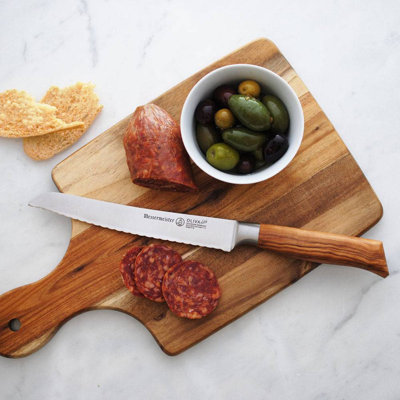 Messermeister Oliva Elite Reverse Scalloped Utility Knife on a wooden board with sausage, olives, and crispbread, showcasing its precision slicing capabilities for charcuterie.