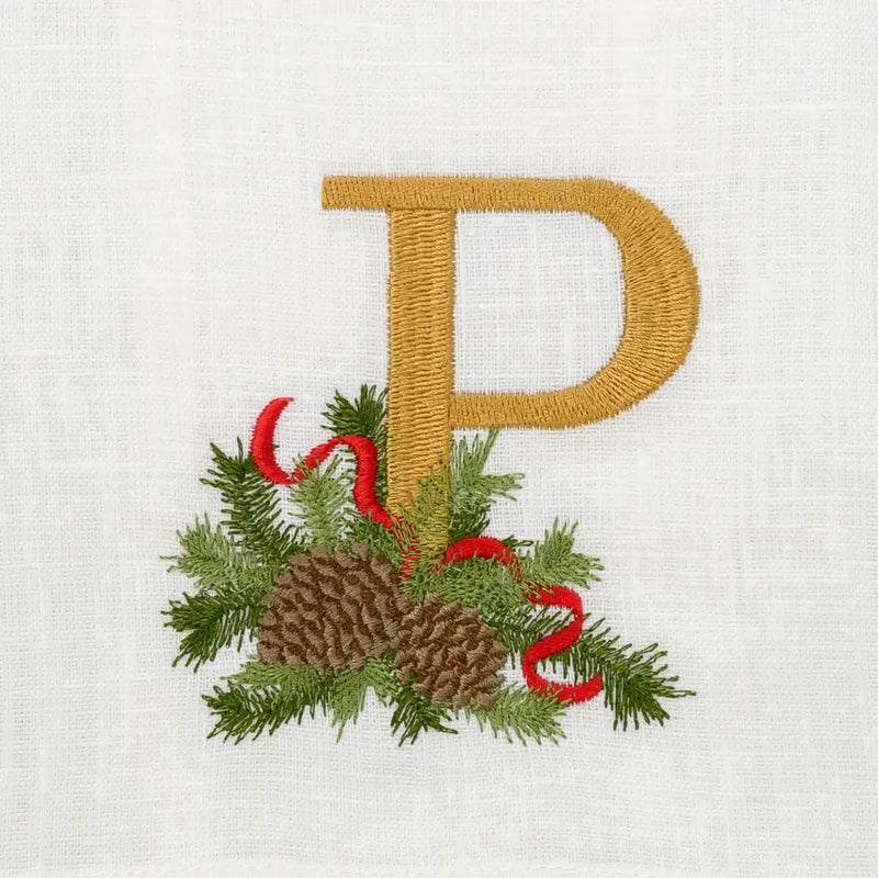 Arte Italica & Crown Linen Designs Winter Pine Monogram Towel with gold P embroidery, accented by evergreen sprigs, pine cones, and red ribbon on white linen.