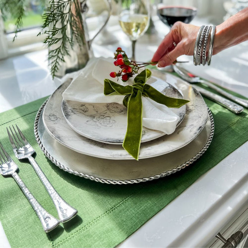 Arte Italica & Crown Linen Designs Hemstitch Placemat - Evergreen set with elegant dinnerware, highlighting a floral plate, velvet-tied napkin, and red berry sprig.