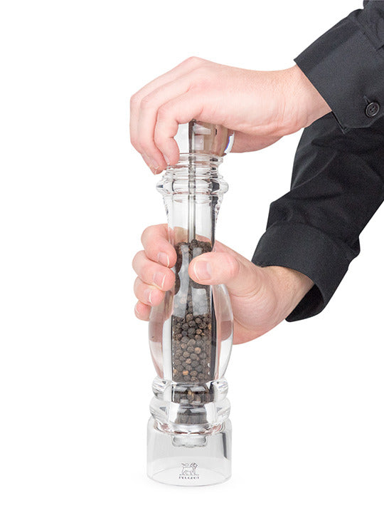 Peugeot | Paris Nancy Pepper Mill, Acrylic, 12 inches, held mid-twist, showcasing black peppercorns inside its clear body, emphasizing elegance and functionality in culinary preparation.
