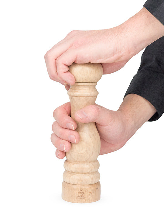 Hands twisting the Peugeot | Paris u'Select Pepper Mill Natural Wood, 9 inches, showcasing its iconic, ergonomic design and durable grinding mechanism against a plain backdrop.