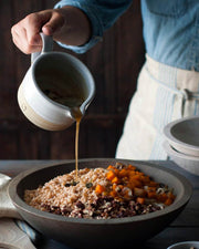 Farmhouse Pottery | Silo Sauce Boat pouring dressing over a rustic grain salad, showcasing its elegant design and practical use in kitchen settings.