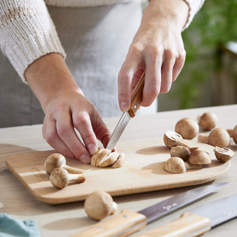 Person using the Opinel | Parallele Trio Chef Knife Set - Olive Wood to slice mushrooms on a cutting board, showcasing the knife's precision and comfort.