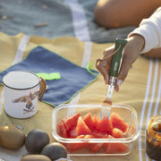 Opinel | No 8 Carbon Steel Folding Knife - Picnic Cutlery+ Set spears watermelon on a picnic blanket, surrounded by fruits and a camping mug.