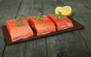 Wildwood Grilling Cedar Grilling Planks with raw salmon and lemon on a wooden board, perfect for infusing smoky flavor into seafood dishes.