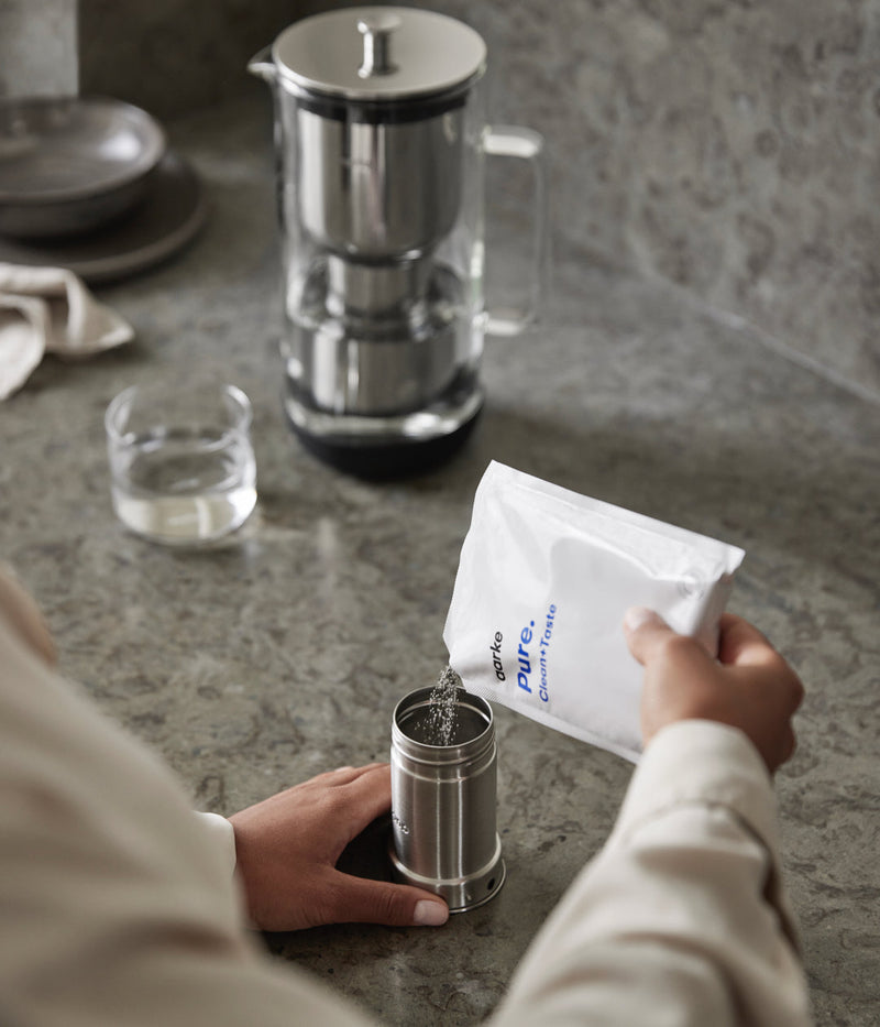 Aarke | Purifier Pure Water Filter Pitcher with refillable steel cartridge being filled with granules, enhancing tap water quality for a cleaner drinking experience.