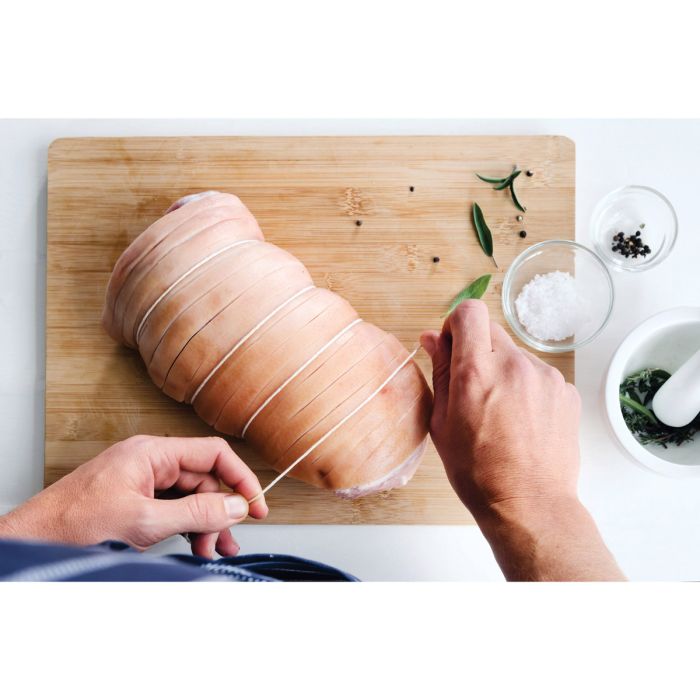 Cooking Twine with Wooden Holder being used to tie a piece of meat, shown alongside a mortar, pestle, and seasoning bowls.