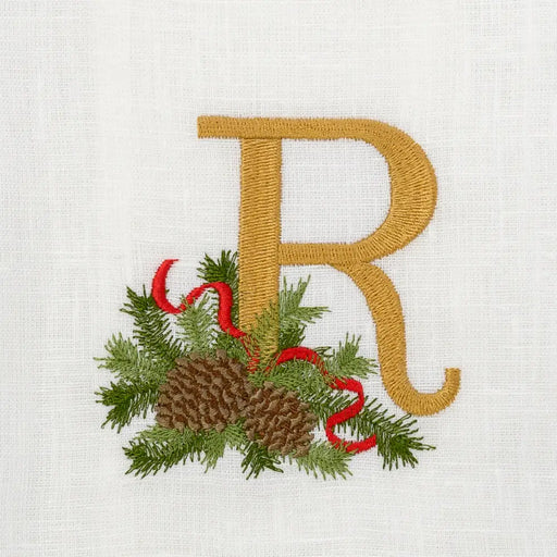 Winter Pine Monogram Towel, R, by Arte Italica & Crown Linen Designs, features embroidered gold letter R with evergreen sprig, pinecones, and red ribbon on linen.