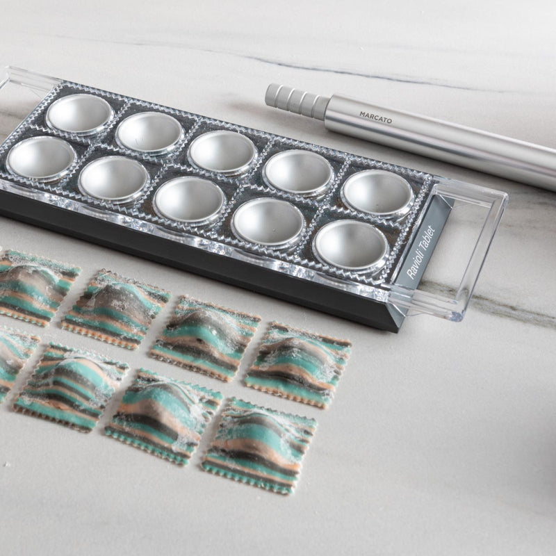 Marcato Ravioli Tablet Pasta Makers (Black) with a tray of neatly arranged square ravioli, accompanied by a pasta rolling pin for easy cutting and sealing.