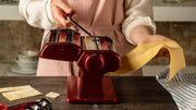 Marcato | Atlas 150 Pasta Maker (Ice) in use, showcasing its manual operation for crafting fresh pasta with a red-handled tool in a kitchen setting.