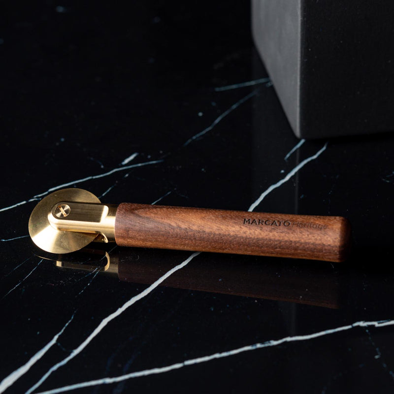 Marcato | Smooth Pasta Wheel Cutter with brass wheel and wooden handle, engraved “MARCATO Heritage,” on dark marble, ideal for precise pasta slicing.