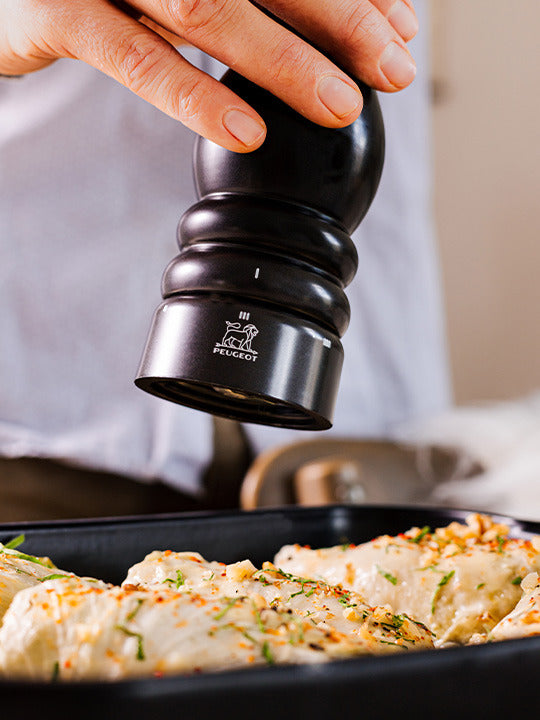 Peugeot | Paris u'Select Wooden Pepper Mill, Satin Black, grinding fresh pepper onto seasoned chicken breasts in a pan, highlighting its ergonomic design and precise grind adjustment.